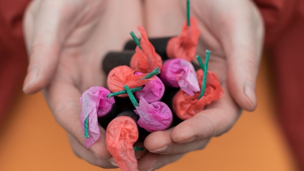 雙手捧著數個用粉色與橘色紙包裝的小型煙火爆竹，露出的引信清晰可見。