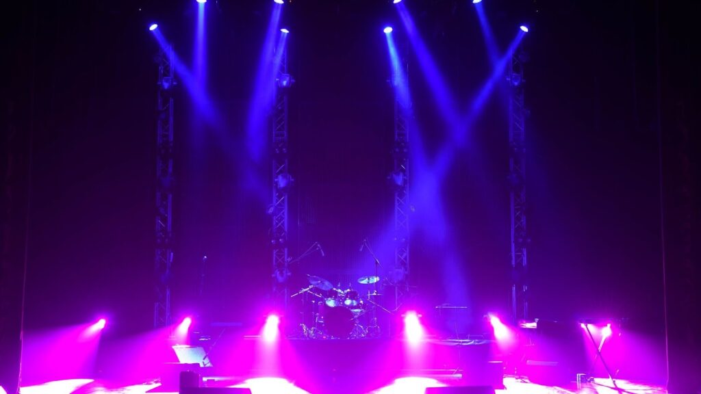 渲染紫藍色調的表演舞台，多組電腦燈投射光束至中央爵士鼓，適合活動場地租借或音響燈光工程展示。