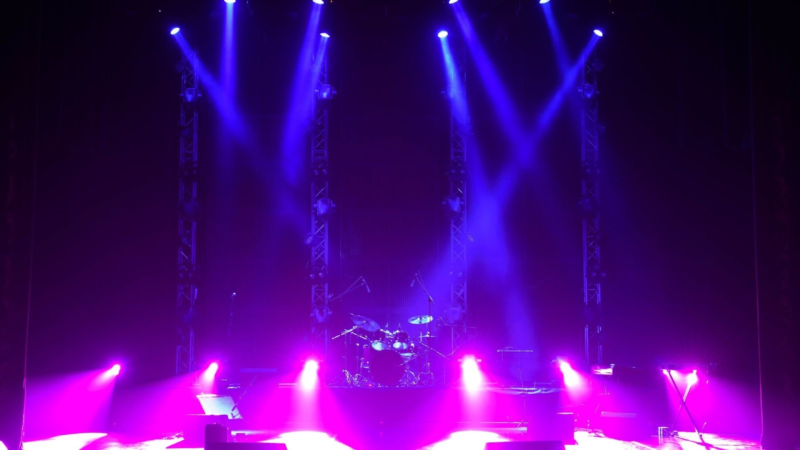渲染紫藍色調的表演舞台，多組電腦燈投射光束至中央爵士鼓，適合活動場地租借或音響燈光工程展示
