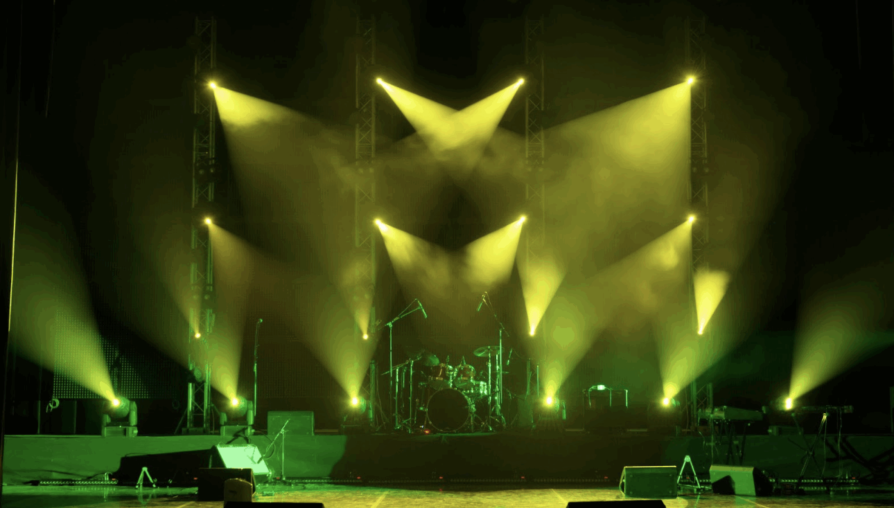 專業表演舞台燈光配置，黃綠色投射燈與煙霧效果，背景可見架設好的爵士鼓與樂器設備。