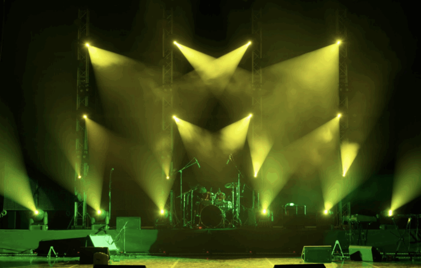 專業表演舞台燈光配置，黃綠色投射燈與煙霧效果，背景可見架設好的爵士鼓與樂器設備。