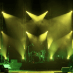 專業表演舞台燈光配置，黃綠色投射燈與煙霧效果，背景可見架設好的爵士鼓與樂器設備