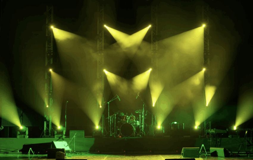 專業表演舞台燈光配置，黃綠色投射燈與煙霧效果，背景可見架設好的爵士鼓與樂器設備