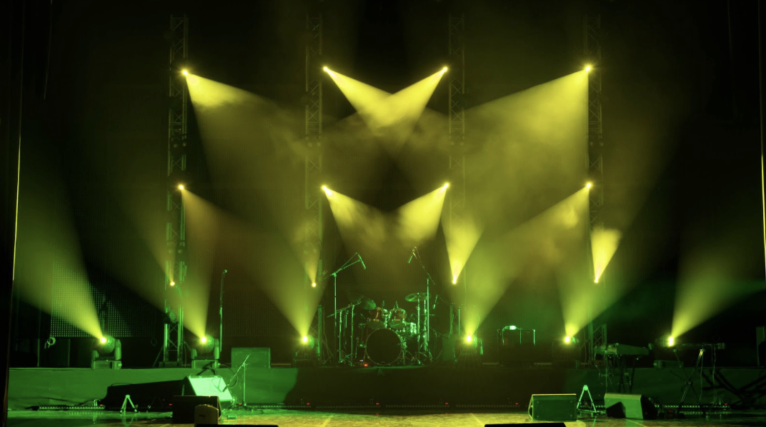 專業表演舞台燈光配置，黃綠色投射燈與煙霧效果，背景可見架設好的爵士鼓與樂器設備